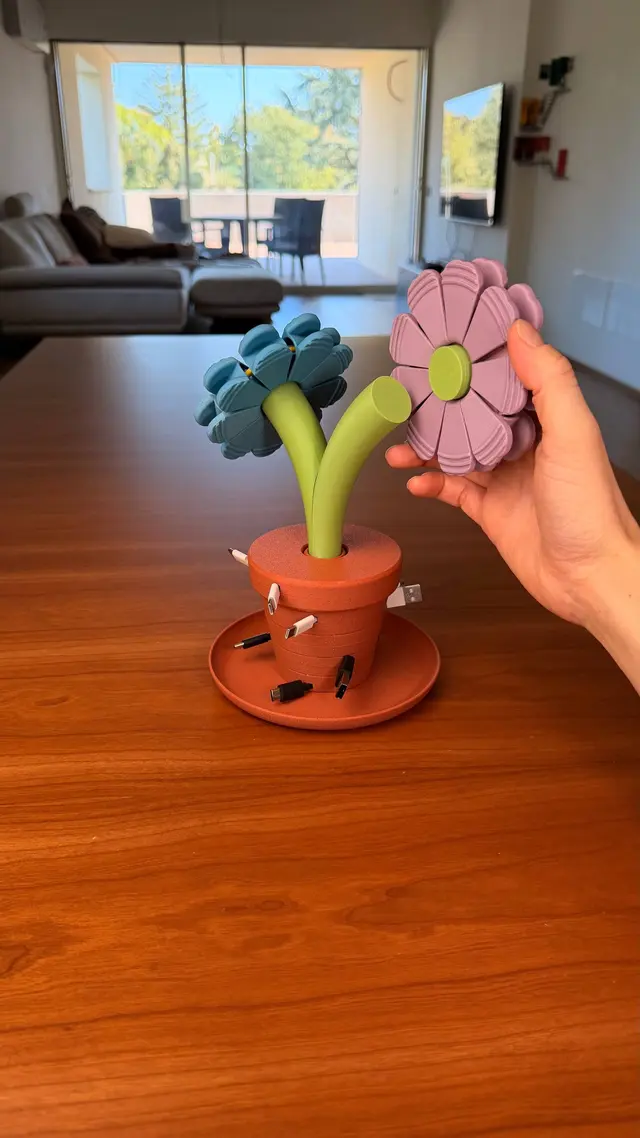 A hand lifts a pink flower next to the Bloom Stack vase, with a light blue flower beside it