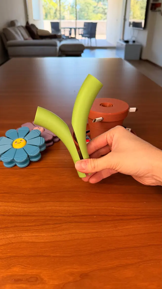 A stem and a light blue flower held in a hand next to the vase