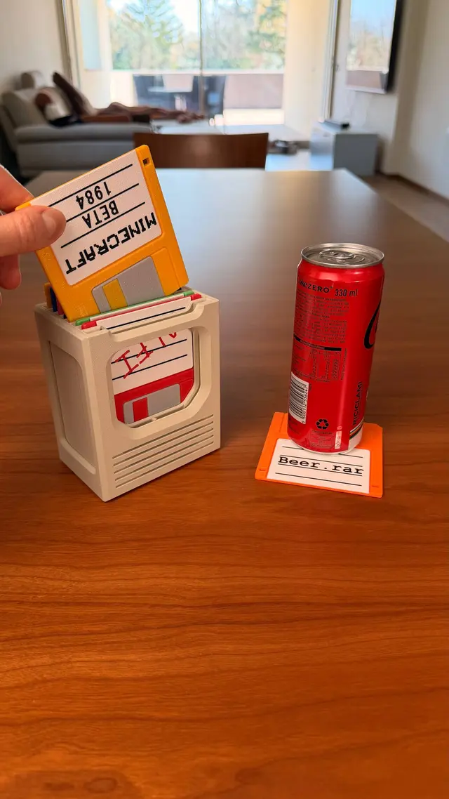 Una mano estrae un floppy giallo dal contenitore; a destra una lattina su un floppy arancione