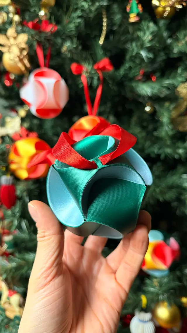 A hand holding the multicoloured Fold Star in front of the Christmas tree