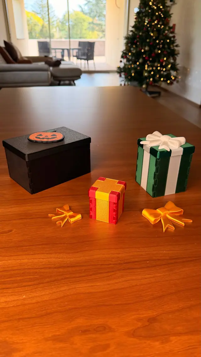 A closed red Gift Reveal with a gold ribbon, between two bows and two bigger boxes