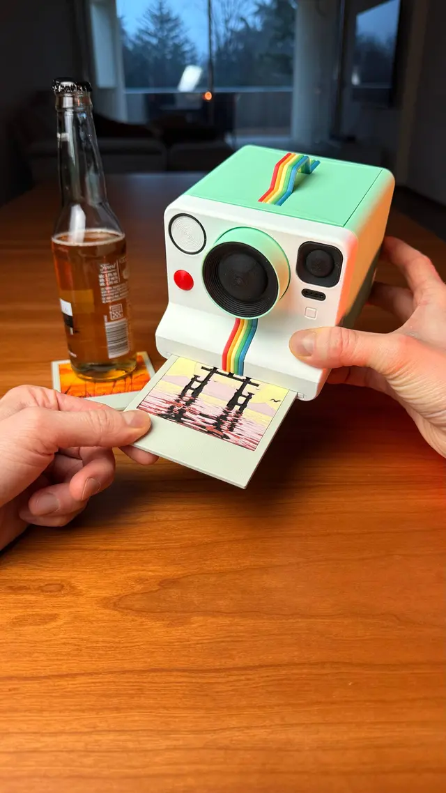 A hand presses the button and a coaster comes out of the camera