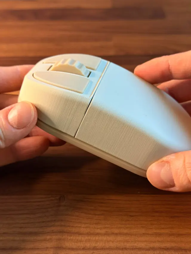 Beige mouse-shaped bottle opener held in two hands, seen from the side, with two buttons and a wheel