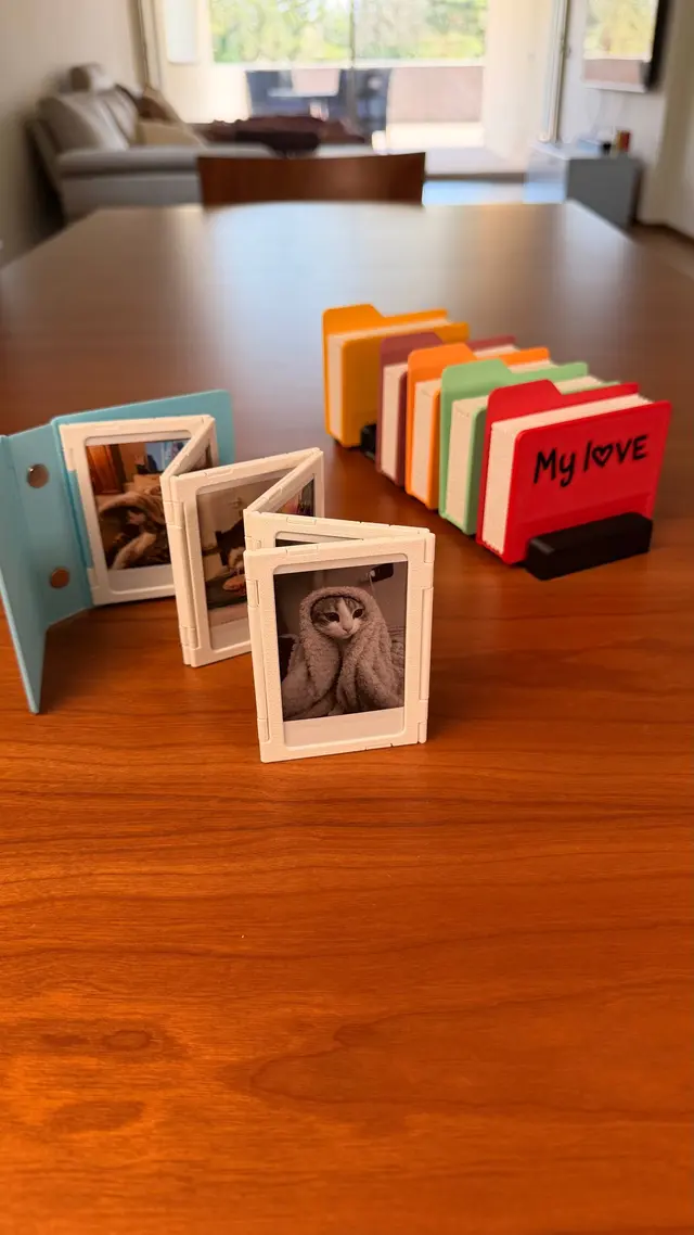 Light blue album open with its white accordion frames and, behind it, five coloured albums in a row on the stand