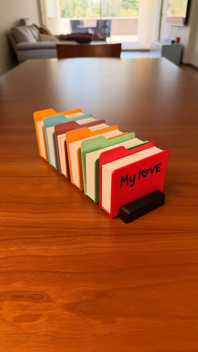 Six folder-shaped albums in several colours lined up on the black stand, the first one red with lettering