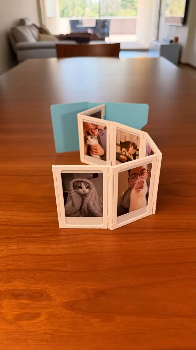 A strip of white frames opened in a zigzag on the table with instant photos, a light blue cover in the background