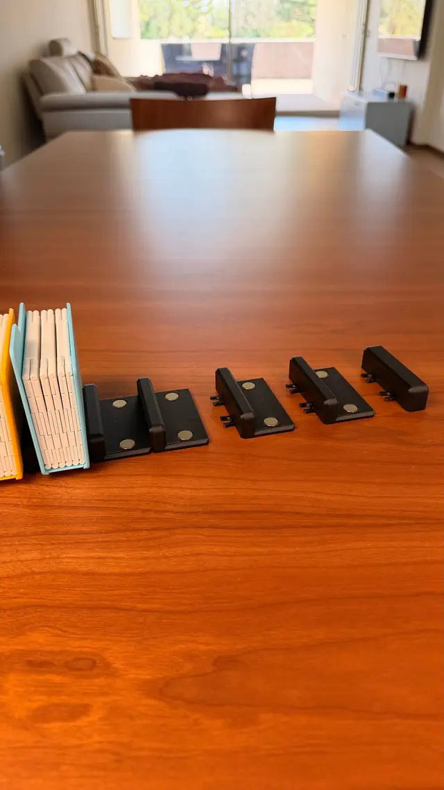 Pieces of the black stand taken apart, with the round magnets and the joining clips, next to two albums