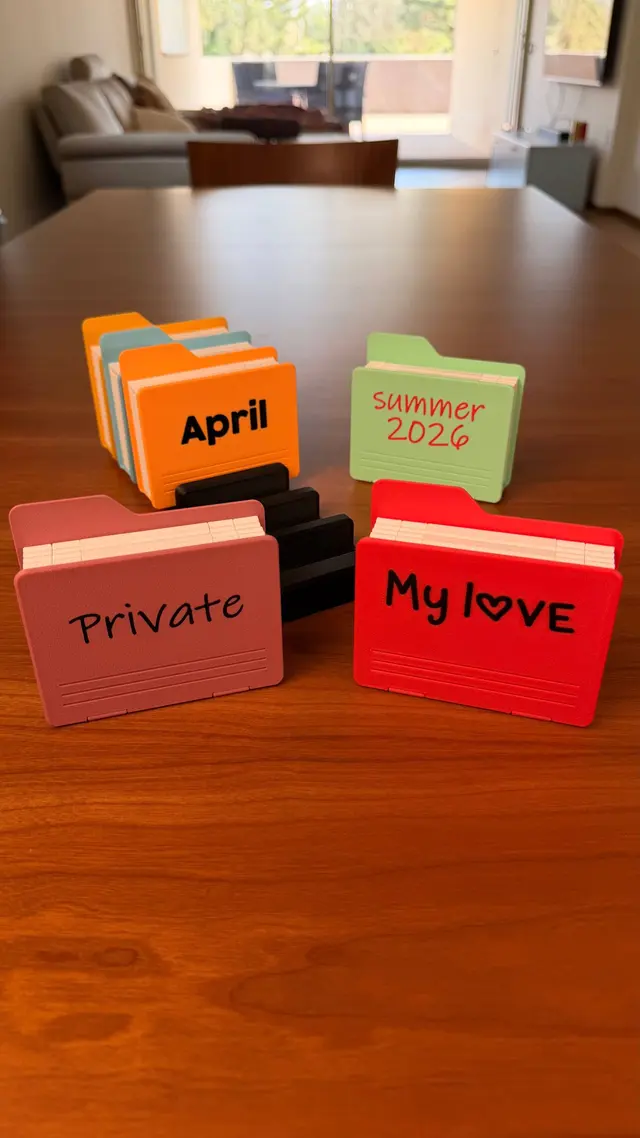 Four closed albums seen from the front, pink, red, green and orange, with coloured raised lettering