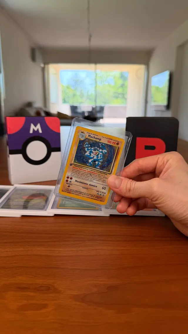 A hand holding a card in a clear rigid toploader, two binders in the background